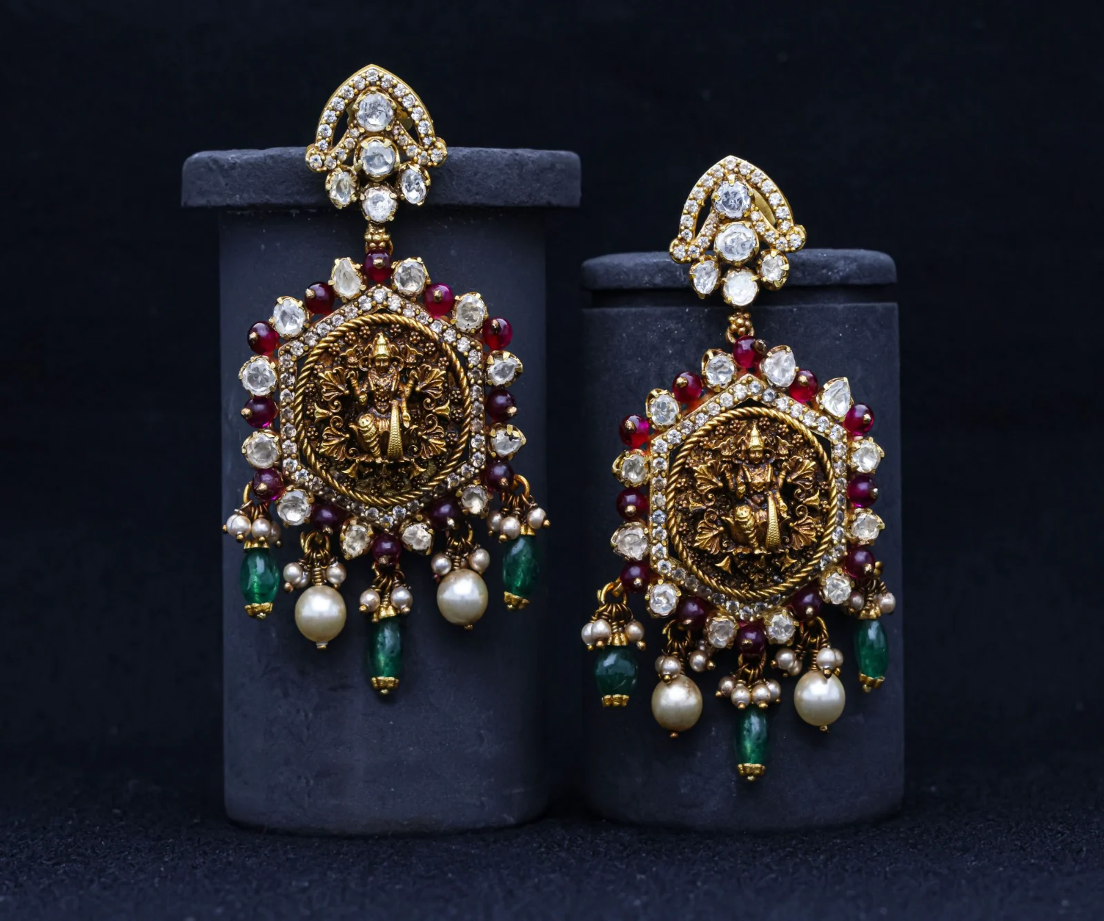 A pair of antique-gold temple earrings with pearl drops hung on two dark stands of different heights
